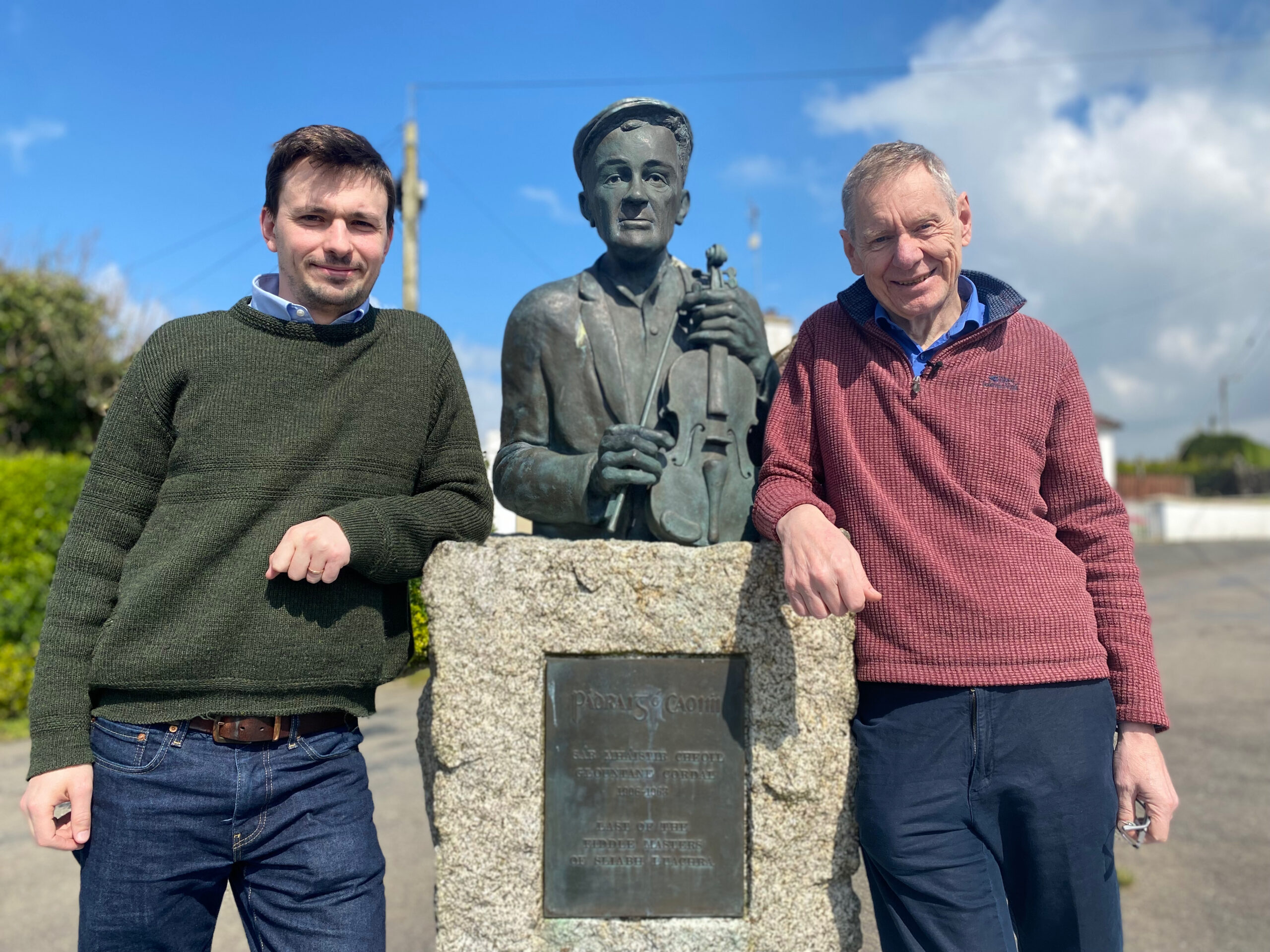 Two men standing with a statue of a man holding a fiddle in between them